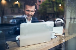 Man wearing a collared shirt typing on a laptop behind a window