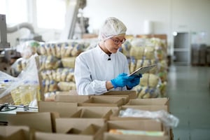 young-professional-female-worker-sterile-cloths-is-using-tablet-inside-factory-storage-room-while-being-leaned-against-boxes
