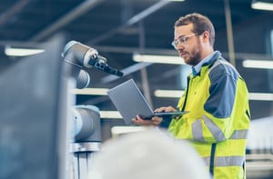 A man looking at a computer near a robot arm