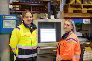 Two smiling industrial professionals by a computer terminal, representing Pinja's digital production expertise
