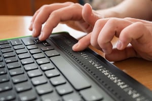 A person's hands using a laptop keyboard with an integrated refreshable braille display at the bottom