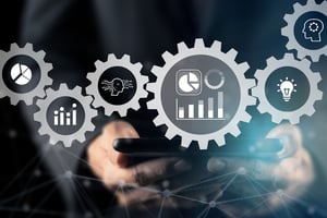 En person som håller i en surfplatta med ett digitalt överlägg av sammankopplade kugghjul som innehåller dataikoner som representerar prestandaoptimering och automatiserad databehandling.